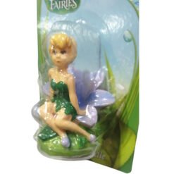 Small plastic fairy figurine in a green dress with purple wings, perched on a leaf inside packaging.