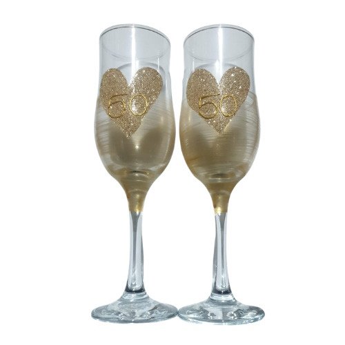 Two champagne flutes with gold glitter hearts displaying 50, set up for a 50th anniversary celebration.