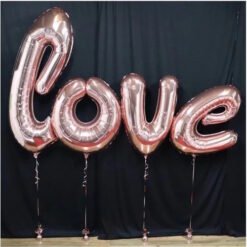 Rose-gold foil balloons spelling 'love' tied to strings against a black backdrop.