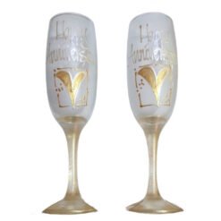 Two champagne flutes with gold “Happy Anniversary” script and heart designs, side by side on a white background.
