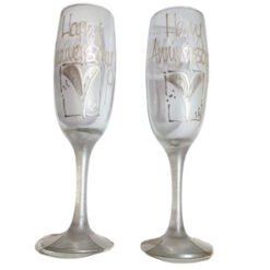 Two champagne flutes with silver engraving reading 'Happy Anniversary' for a celebration.
