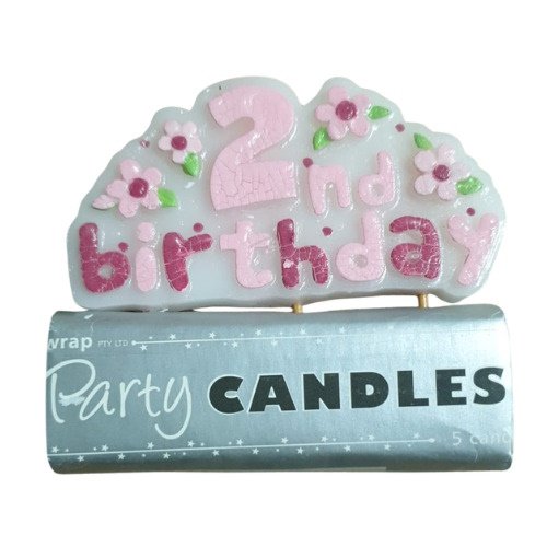 Pink and white '2nd birthday' cake topper with flower accents resting on a blue 'Party Candles' package.